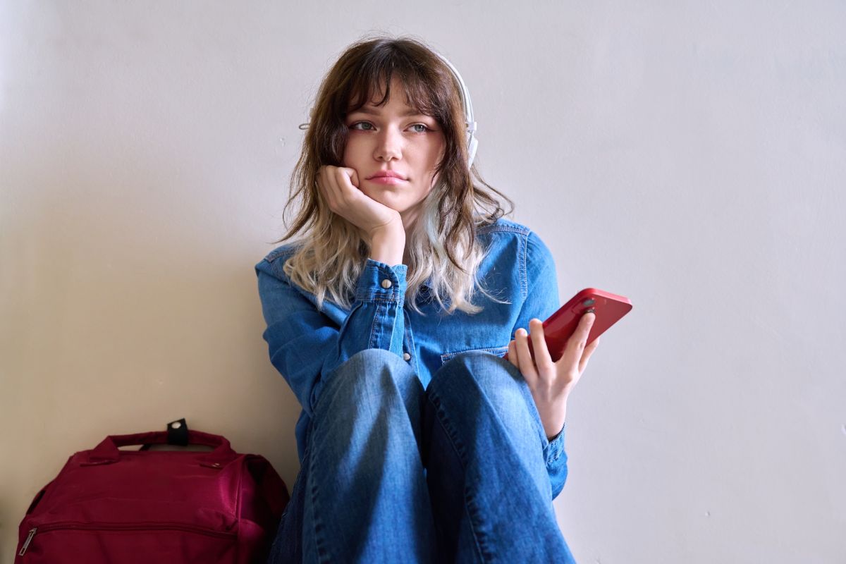 Sad girl sitting on the floor with headphones on and a phone in her hand.