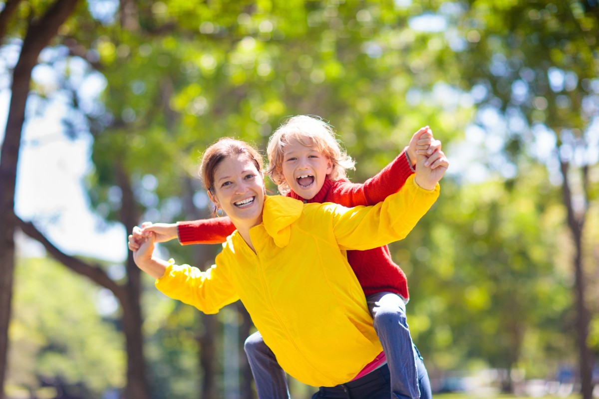 Smiling woman outdoors with a happy child on her back.