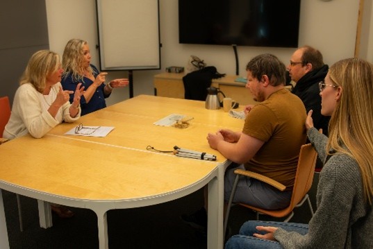 En grupp personer sitter runt ett bord i ett möte och deltar i en diskussion.