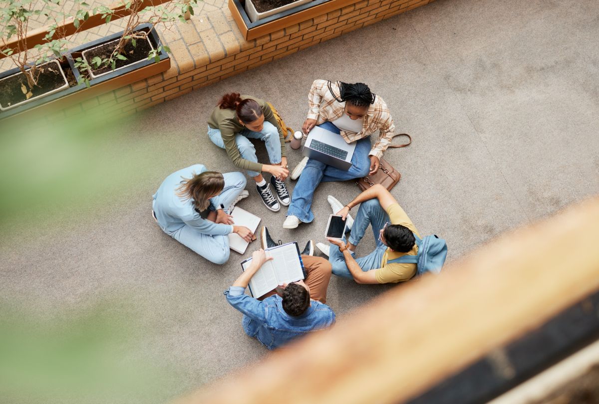 Five young persons sitting on the ground in a circle with laptops