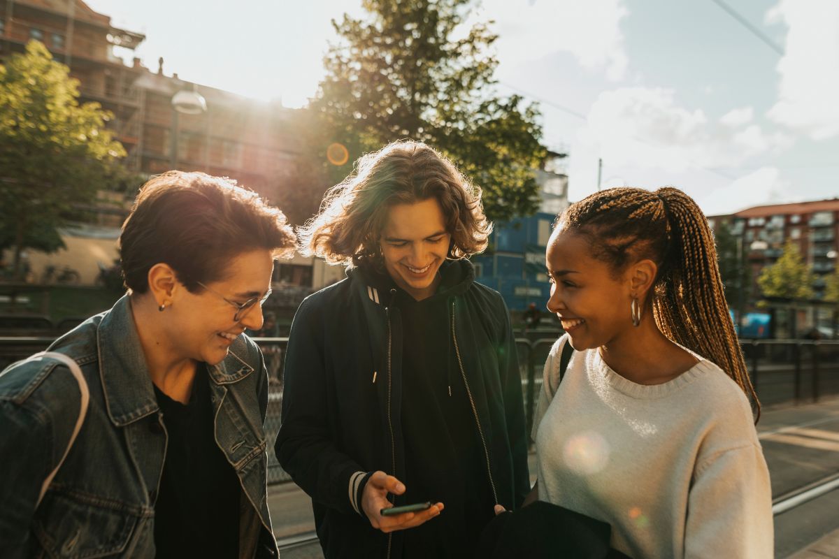 Smiling young man using a smart phone while standing with friends on a street