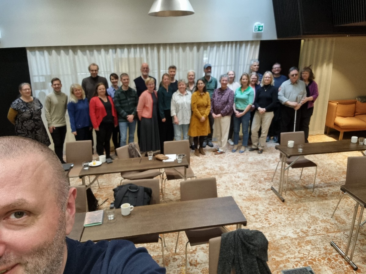 En gruppe på 25 personer står på rad og ser mot kameraet, med en mann i forgrunnen.