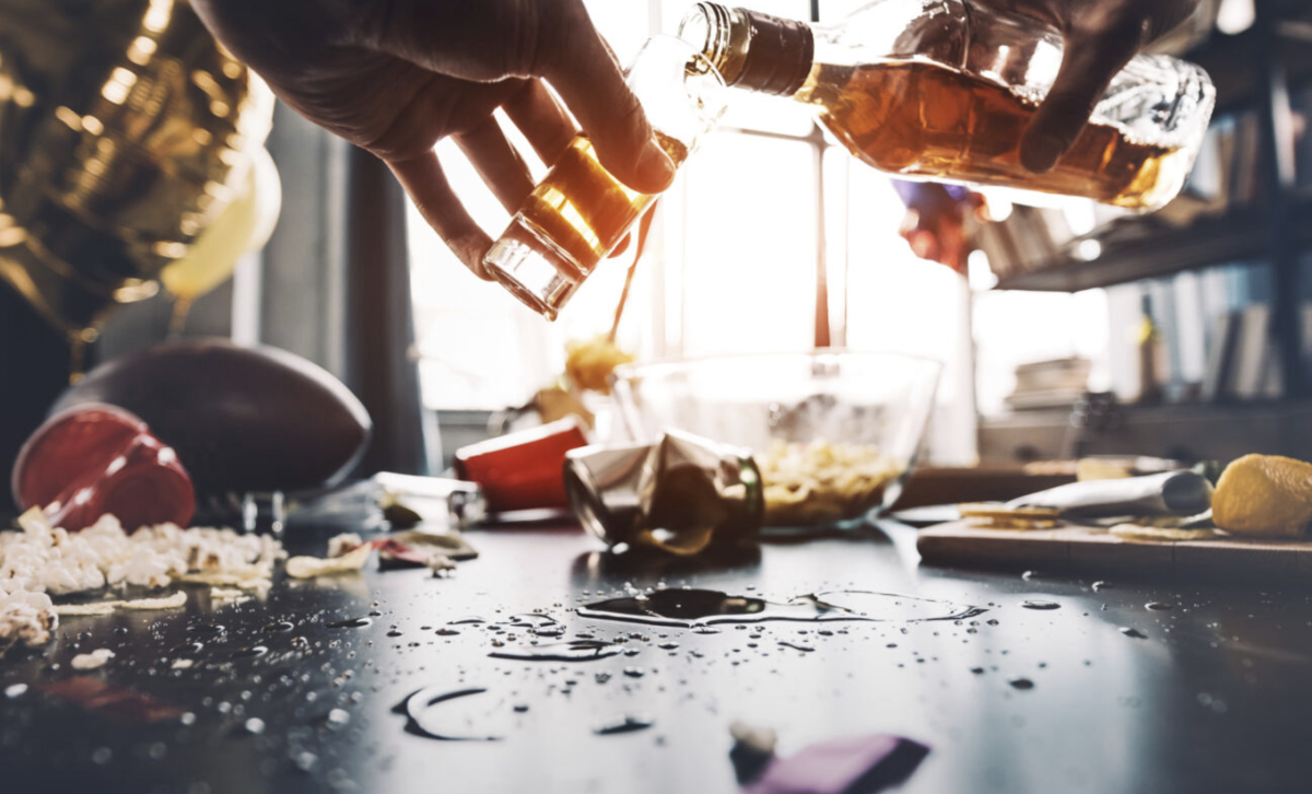 Hand poring a drink in a glass over a messy table.