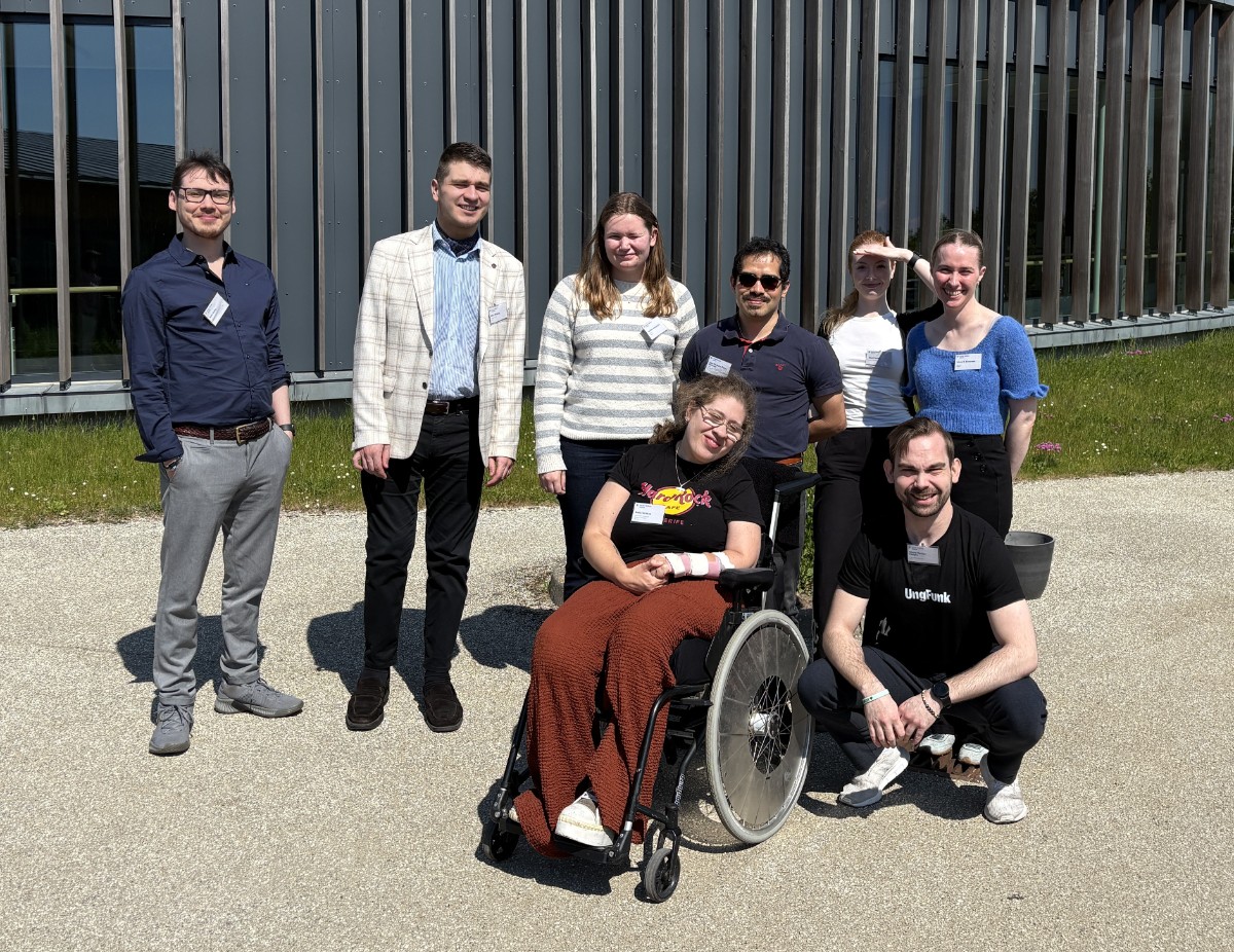 Gruppbild med 8 personer utomhus i solen på Musholm, Danmark. En sitter i rullstol.