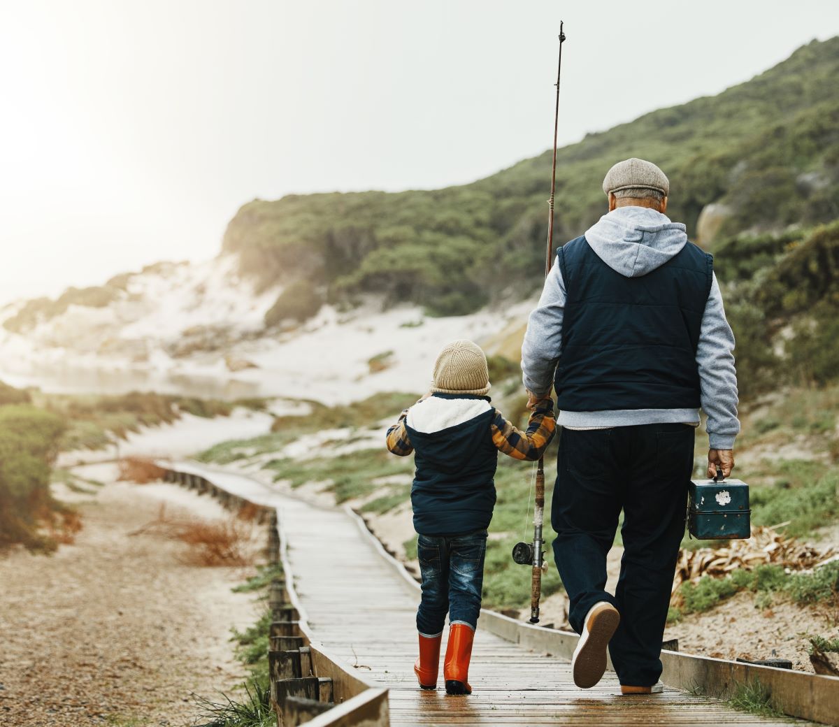 Young child walking hand in hand with an older man on their way fishing.