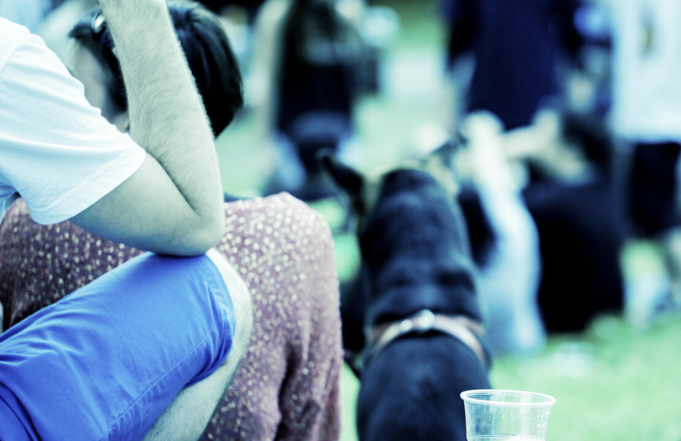 Young man with a plastic cup of drink sitting outdoors among people.