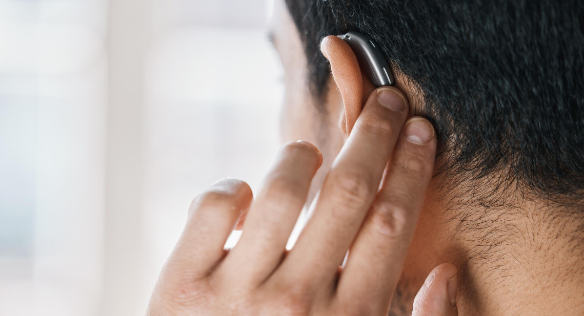 Närbild på en person som justerar en hörapparat bakom örat.