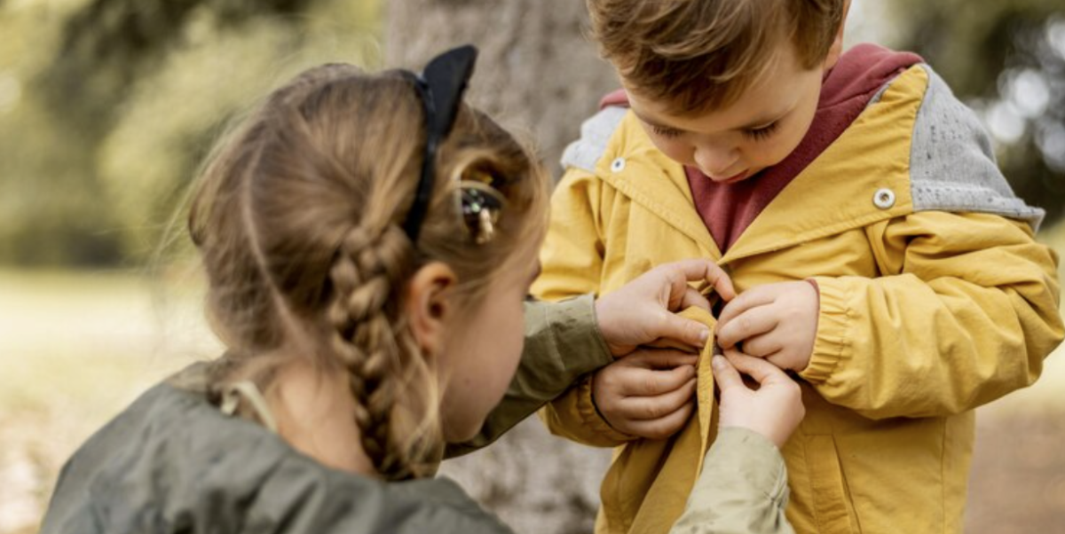 Young girl helping a small boy putting on his jacket.