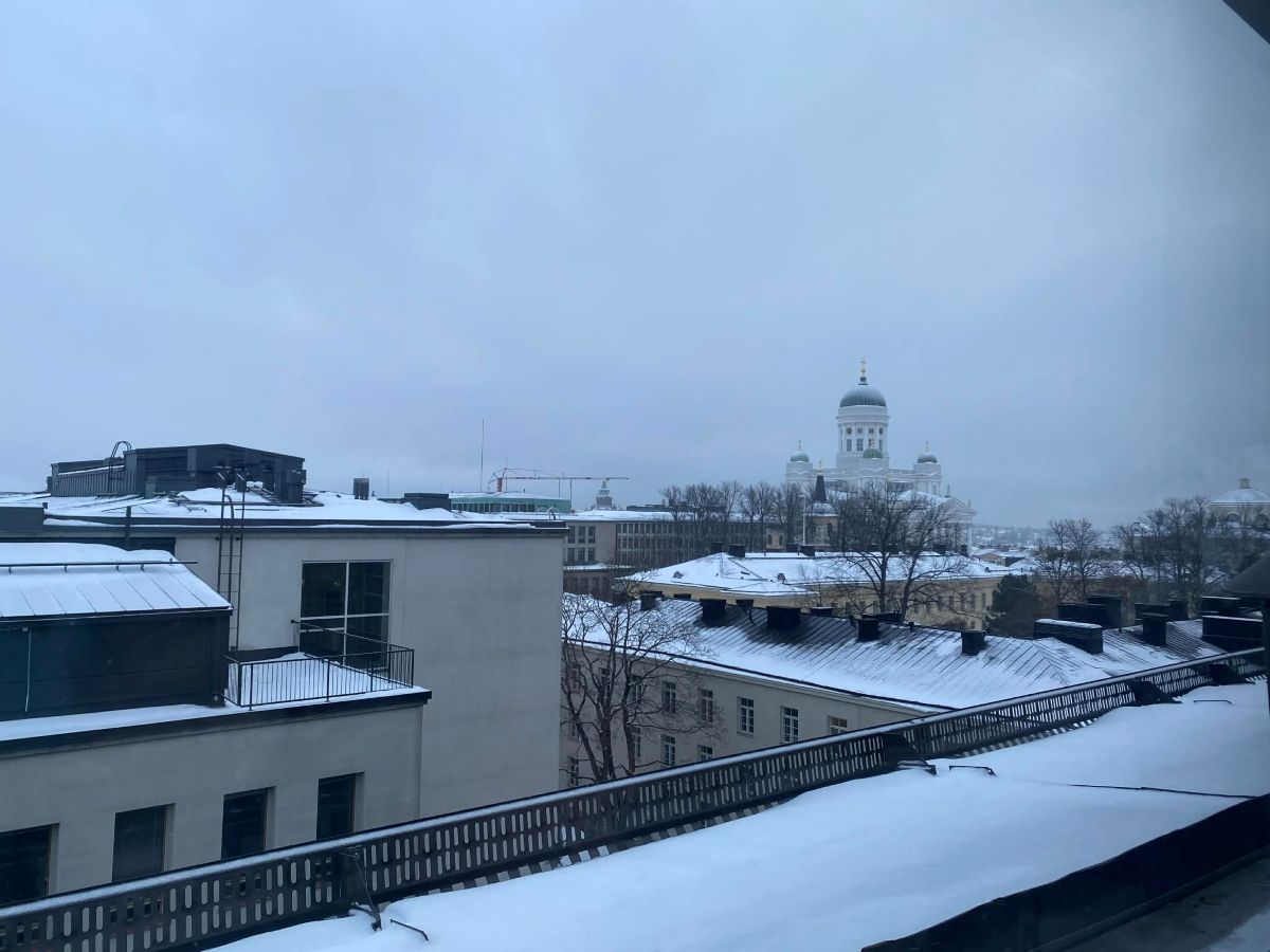 Utsikt över snöiga tak i Helsingfors med domkyrkan i bakgrunden.