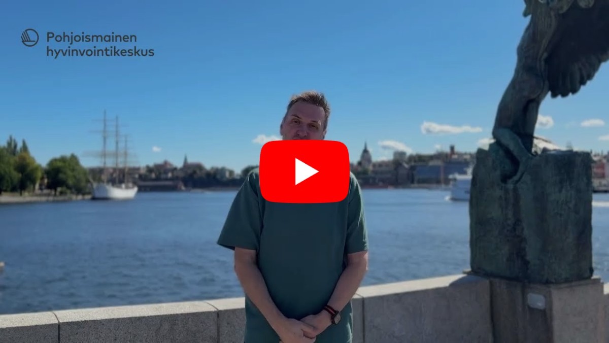En man sitter vid ett litet bord med en tavla med texten ”Stockholm” på väggen bakom sig. Juldekorationer har lagts till i bilden, bland annat grangrenar med ljus högst upp, en samling inslagna paket på bordet framför honom och en tänd adventsljusstake på bordet bredvid.